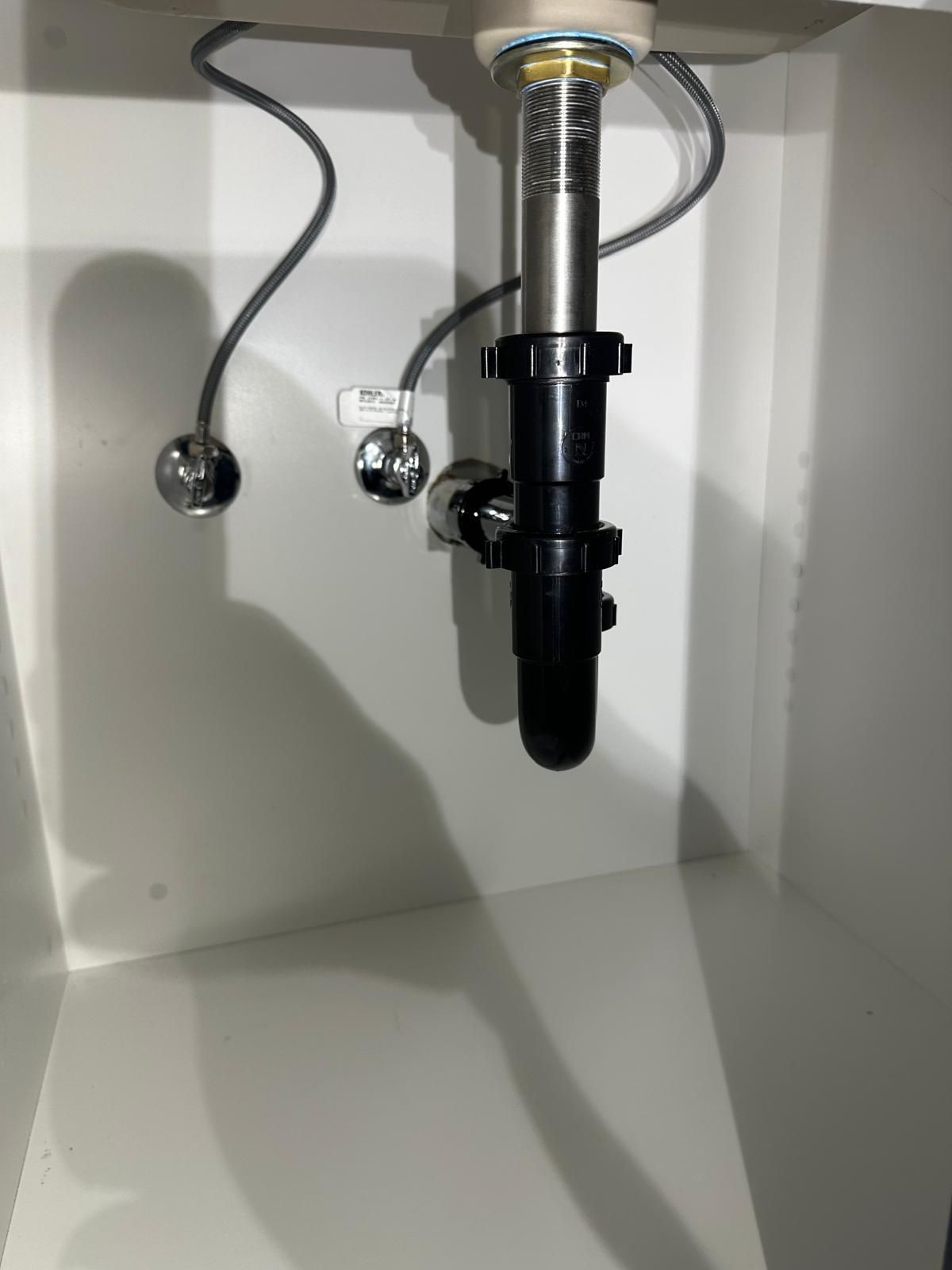 Newly fitted P-trap and braided supply lines under a kitchen sink, left clean and square