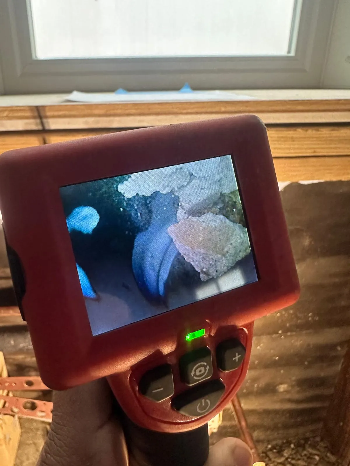 Inspection camera monitor held in one hand showing the inside of a pipe on its screen