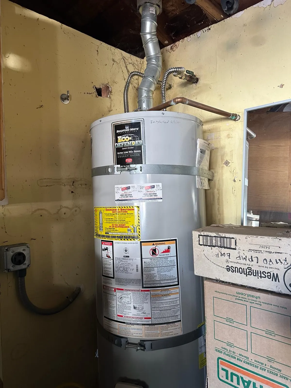 Gas water heater in a garage with earthquake straps, code labels and the install date written on the tank